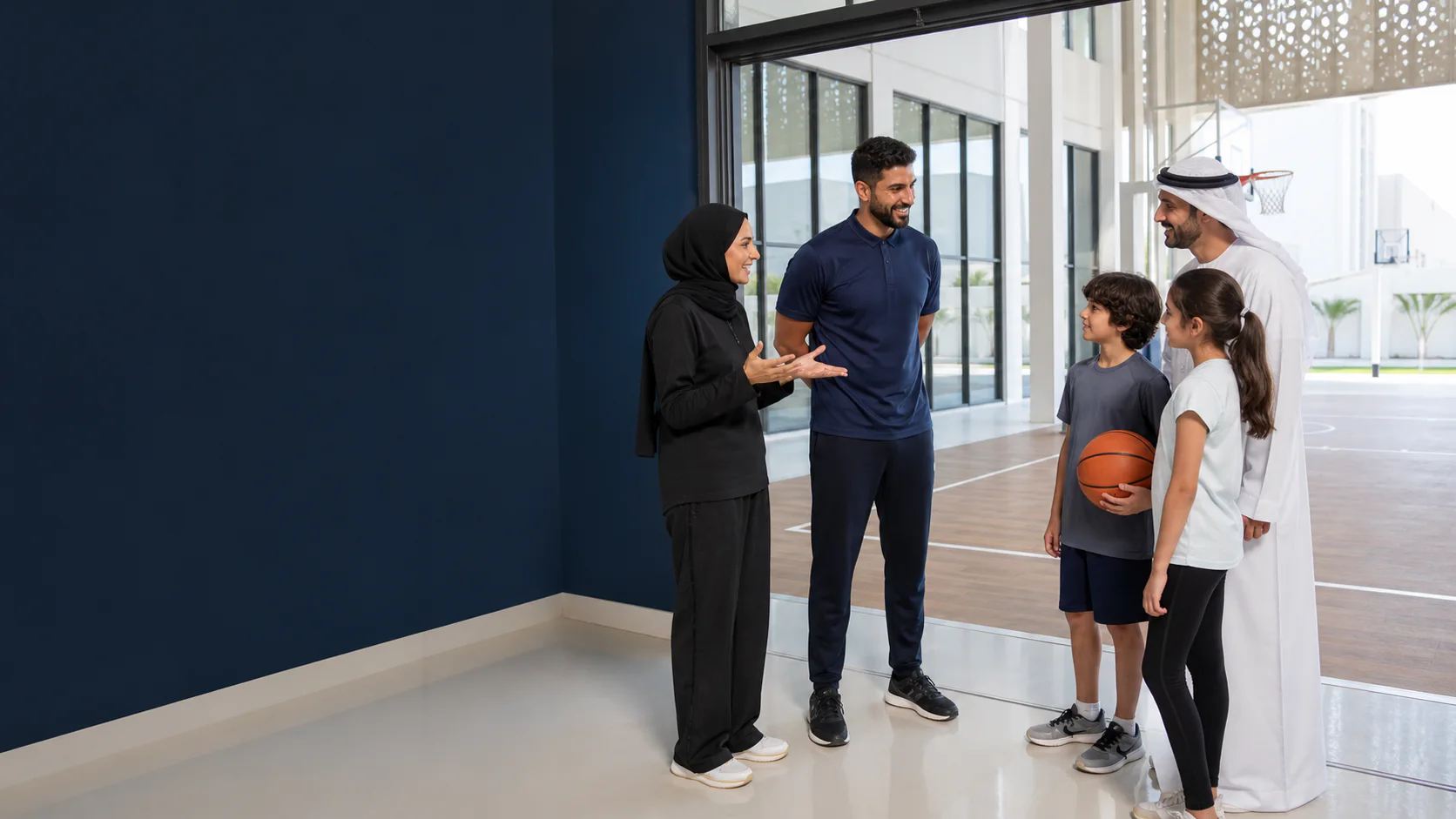 Professional coaches welcoming a parent and children beside an Abu Dhabi school sports court